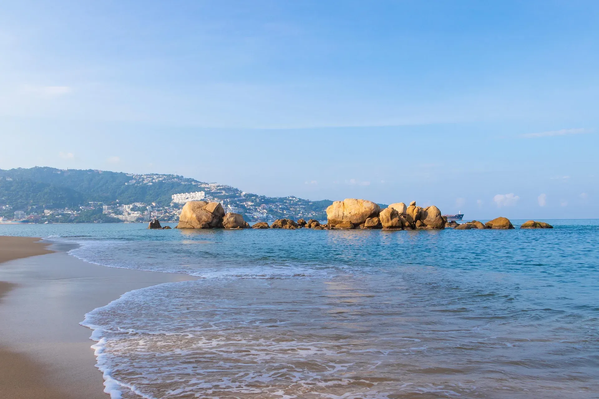 Playa con formaciones rocosas doradas y bahía de Acapulco al fondo