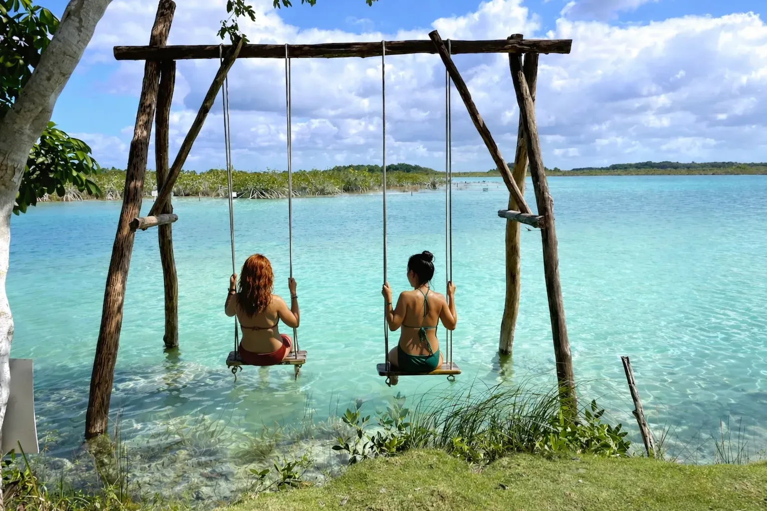 Columpios de madera en las aguas turquesas de Cocalitos con la laguna de Bacalar al fondo
