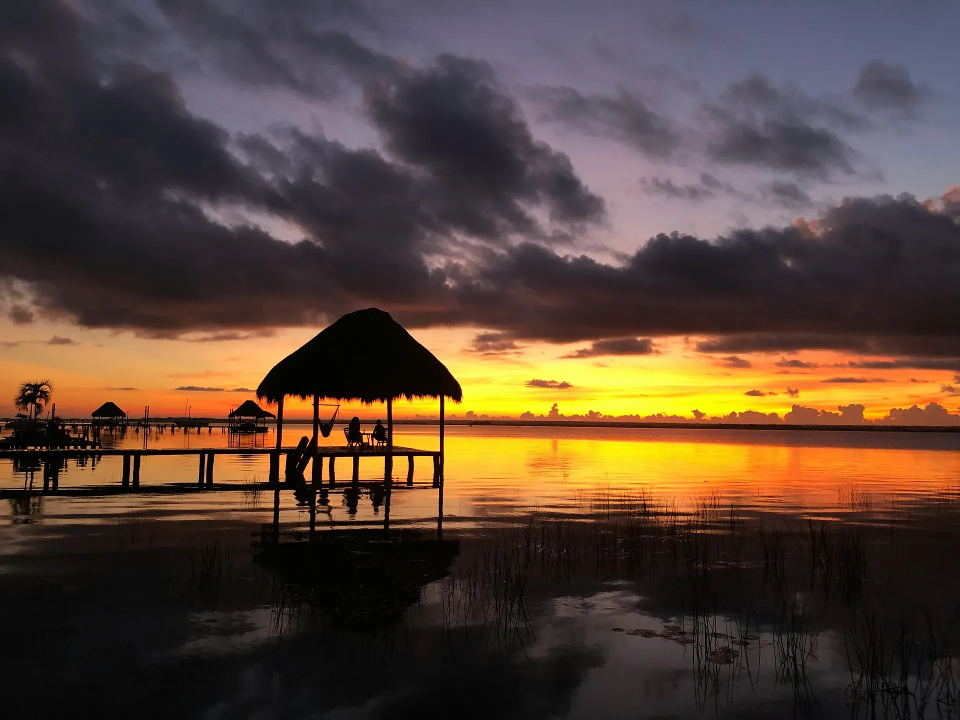 Atardecer espectacular sobre la laguna de Bacalar con silueta de palapa y muelle