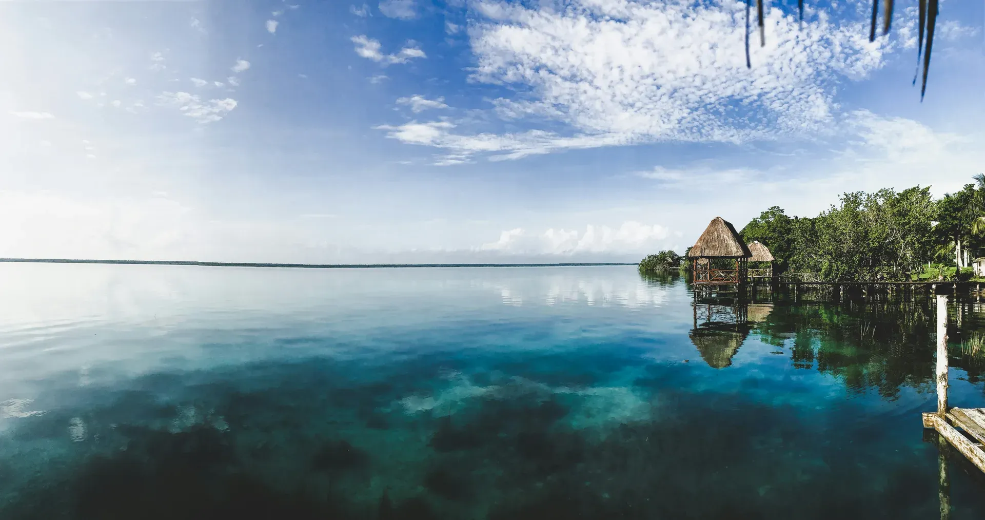 Palapas de palma sobre laguna cristalina de Bacalar con reflejos perfectos