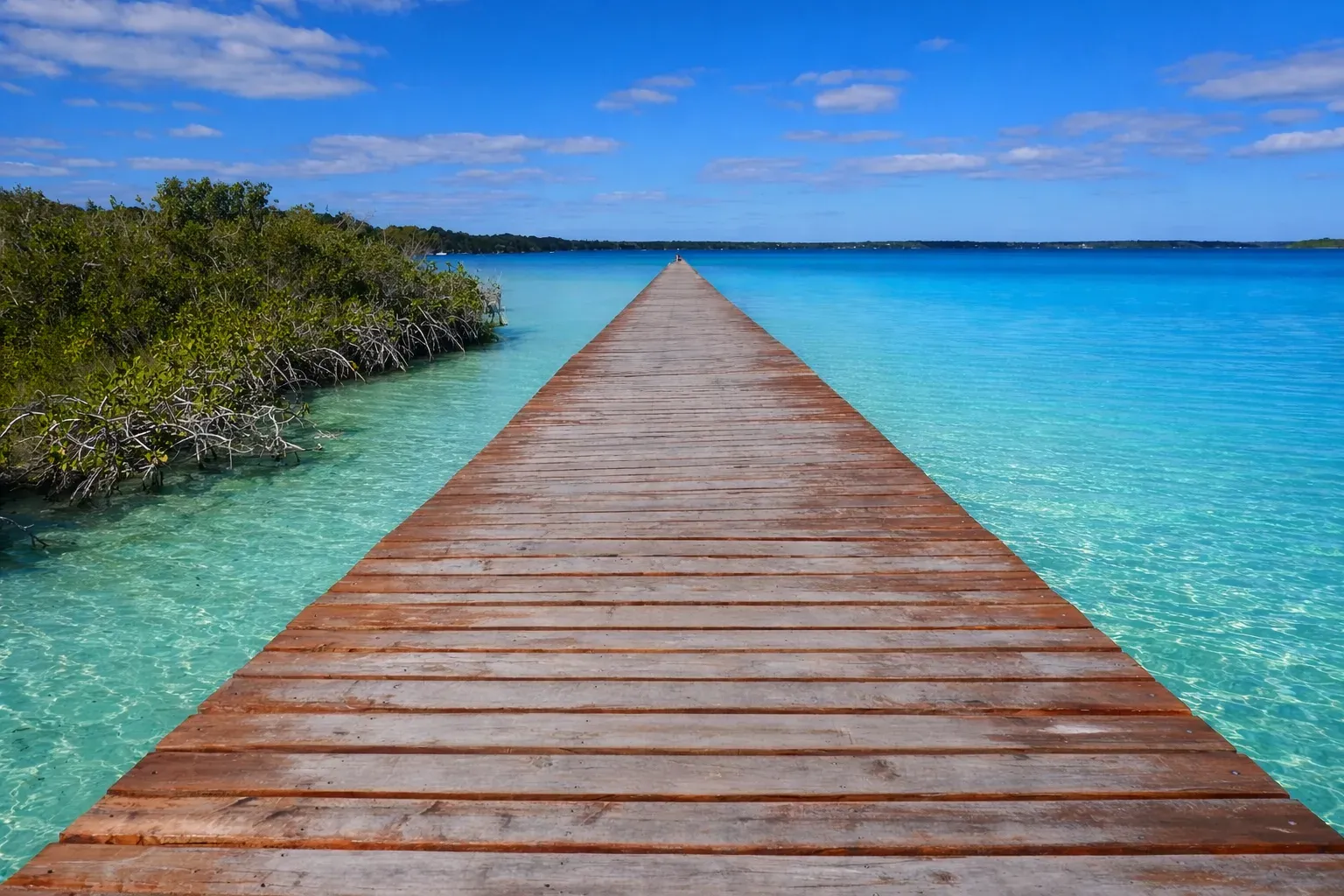 Muelle de madera que se extiende hacia la laguna turquesa de Bacalar entre manglares