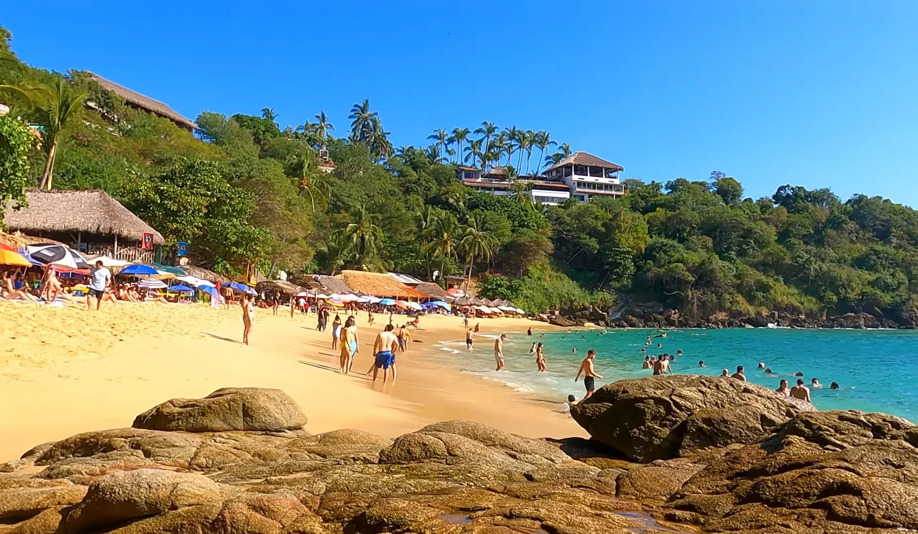 Playa Carrizalillo con rocas, palmeras y gente bañándose