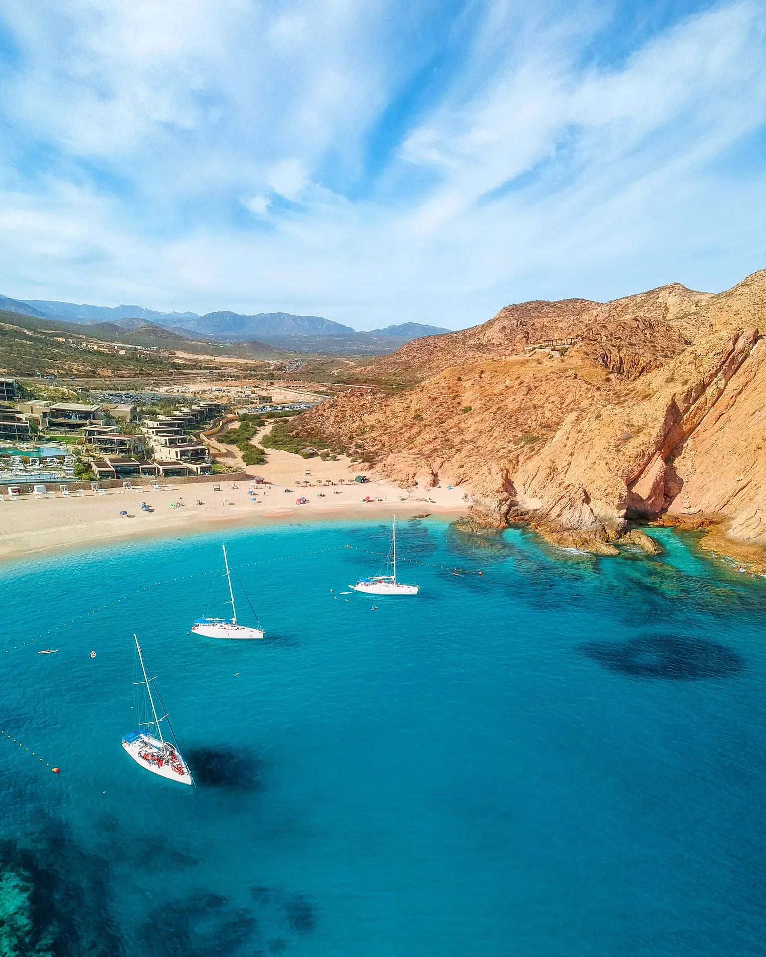 Vista aérea de Playa Santa María con bahía en herradura, veleros y aguas turquesa en Los Cabos