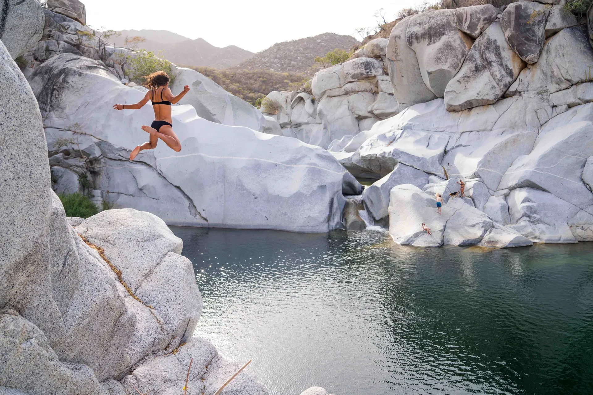 Persona saltando a una poza natural entre rocas blancas en el Cañón de la Zorra, Sierra de la Laguna