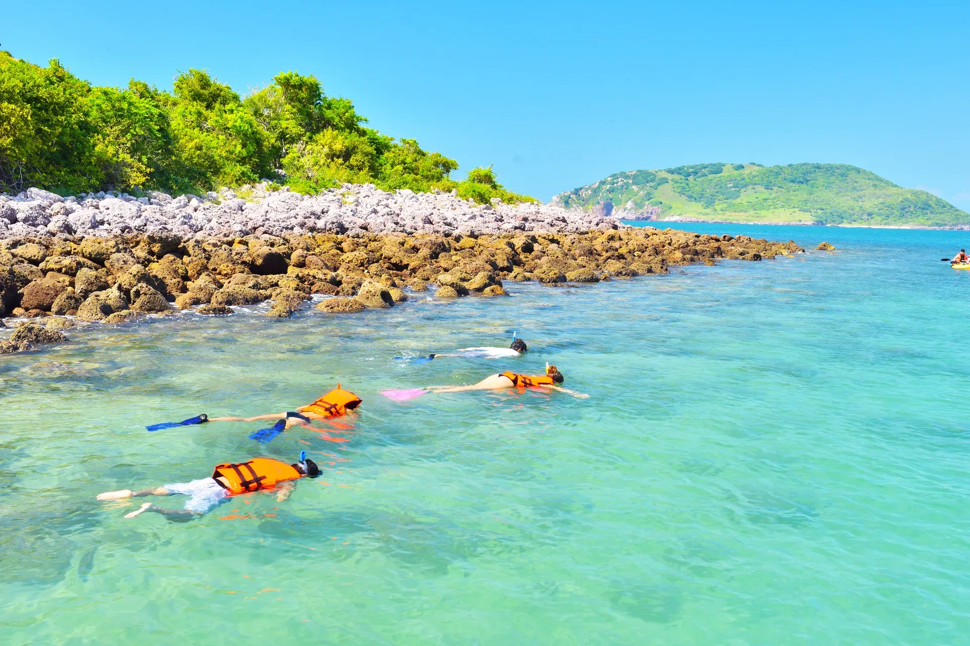 Snorkelistas con chalecos naranja en aguas turquesas junto a la costa rocosa de Isla Venados