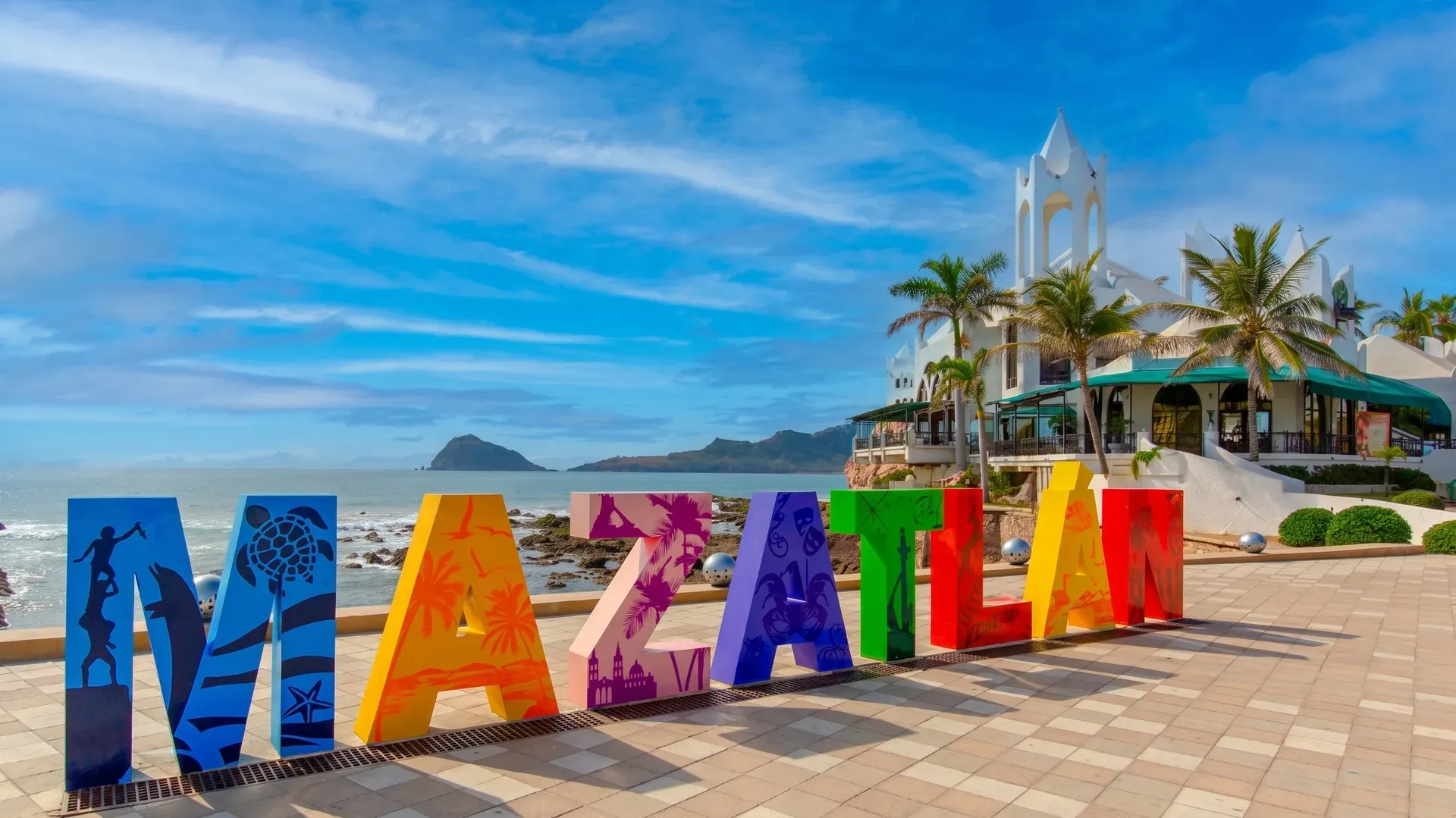 Letras coloridas de MAZATLÁN en el malecón con islas y edificio Valentino de fondo