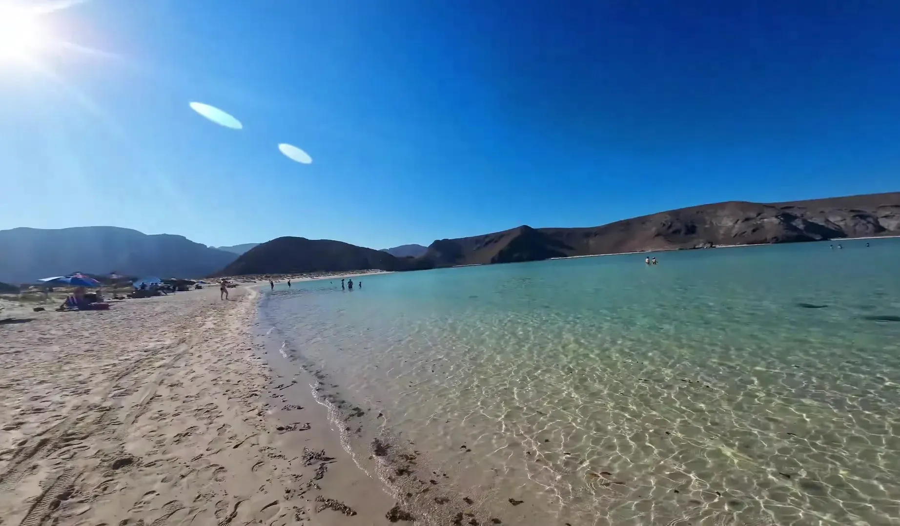 Aguas turquesas someras de Playa Balandra con arena blanca y desierto al fondo