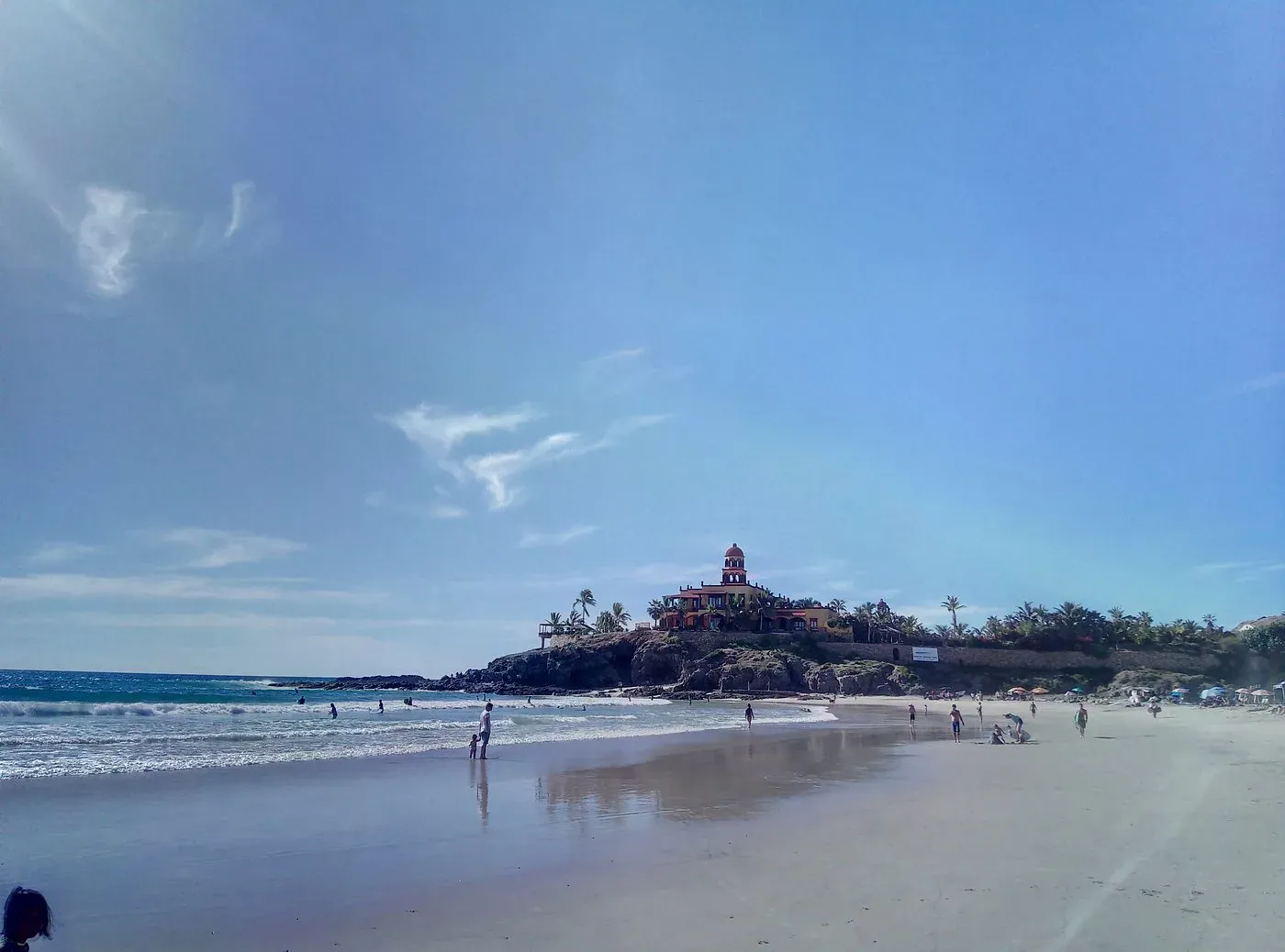 Playa Los Cerritos de día con surfistas y edificio sobre el promontorio