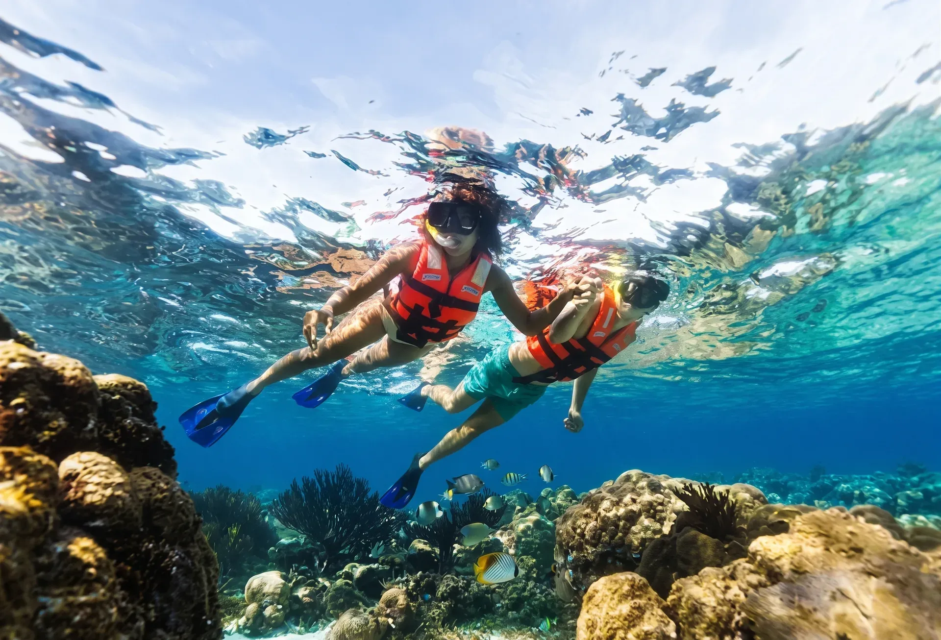 Pareja haciendo snorkel sobre arrecife de coral con peces tropicales en aguas cristalinas