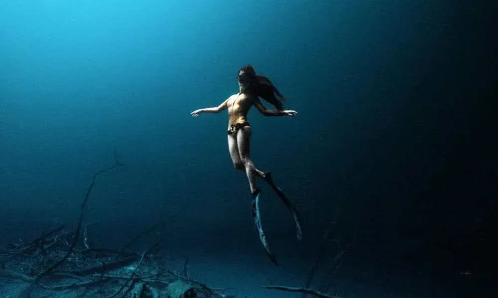 Buceadora flotando en las profundidades azules de un cenote en Tulum